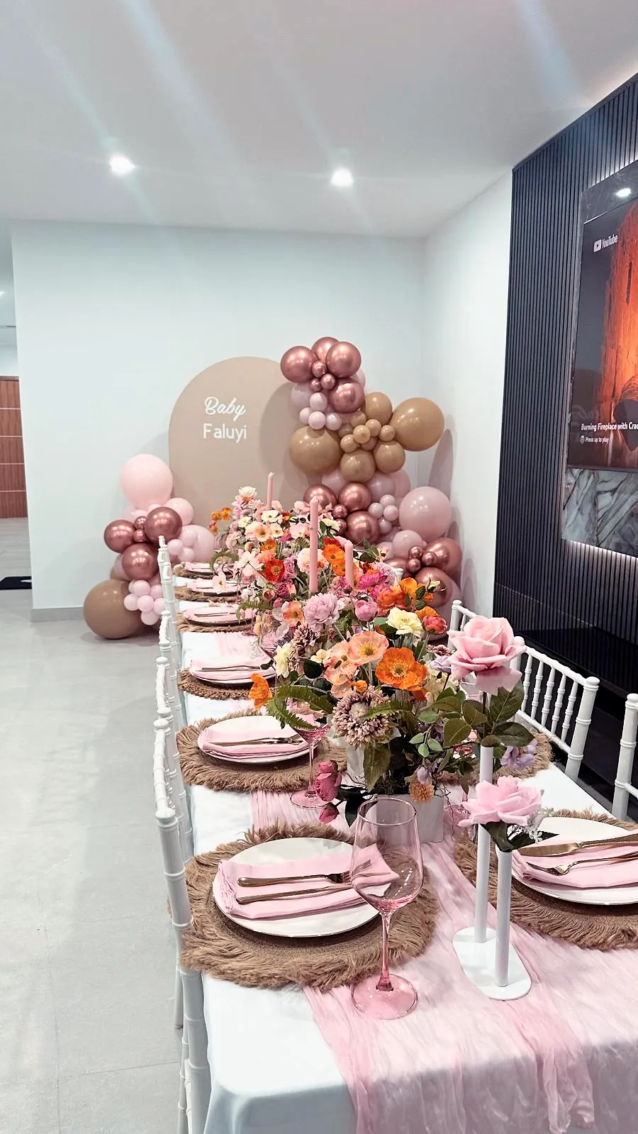 Baby shower table with blush, peach and rose balloons, pink florals and pink napkins in front of a named backdrop