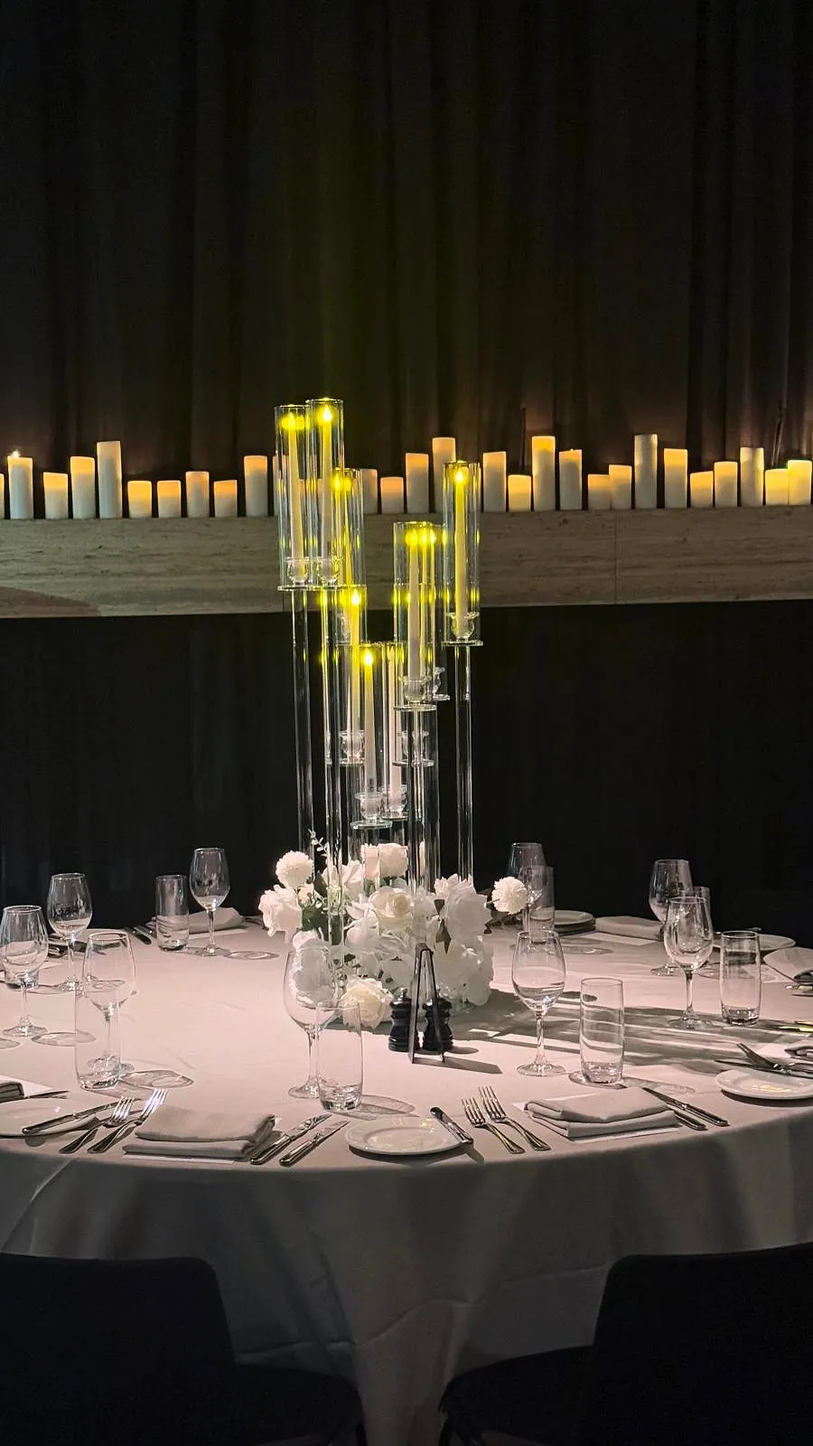 Candlelit reception with tall glass candelabra and white florals, a wall of candles behind