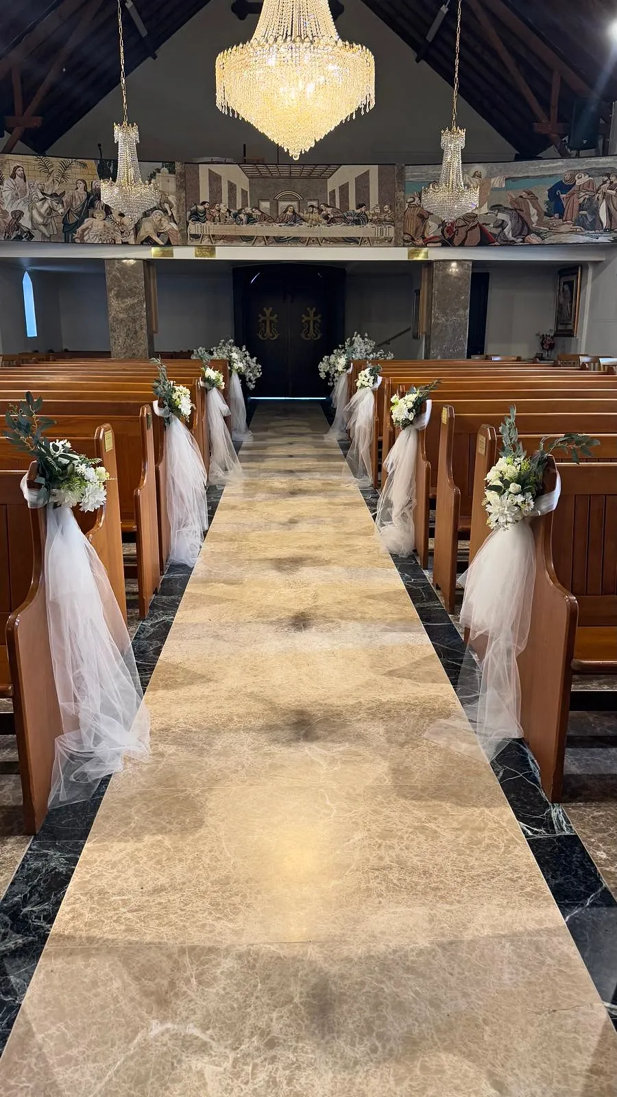 Church aisle styled with white florals and tulle on each pew